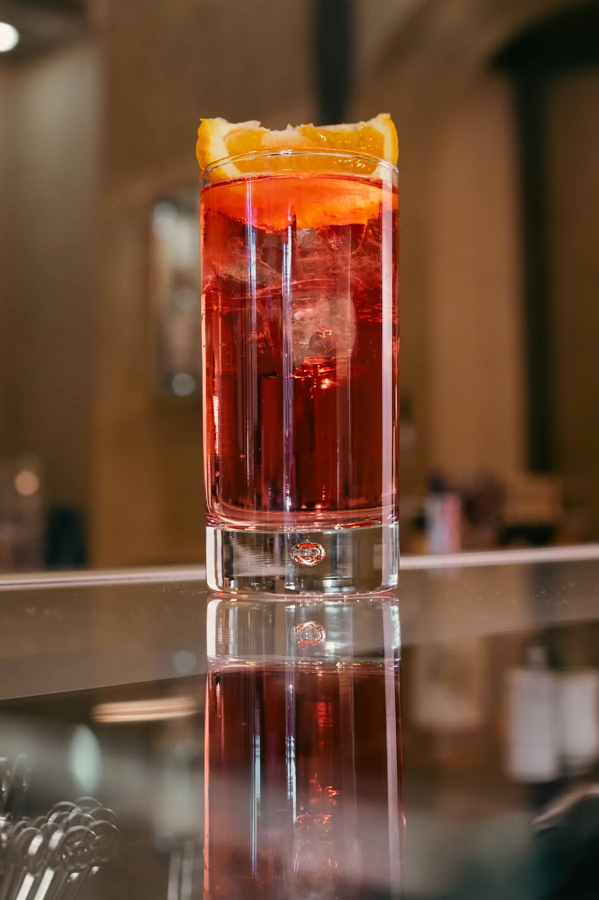 A red cocktail with ice and a slice of orange on the counter