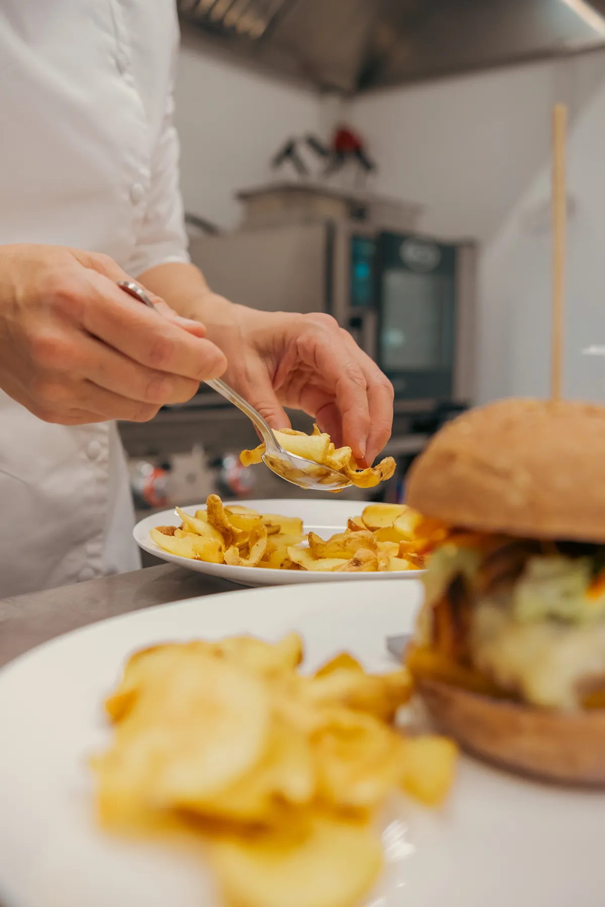 In the kitchen: potato chips being arranged on the plate next to the burger
