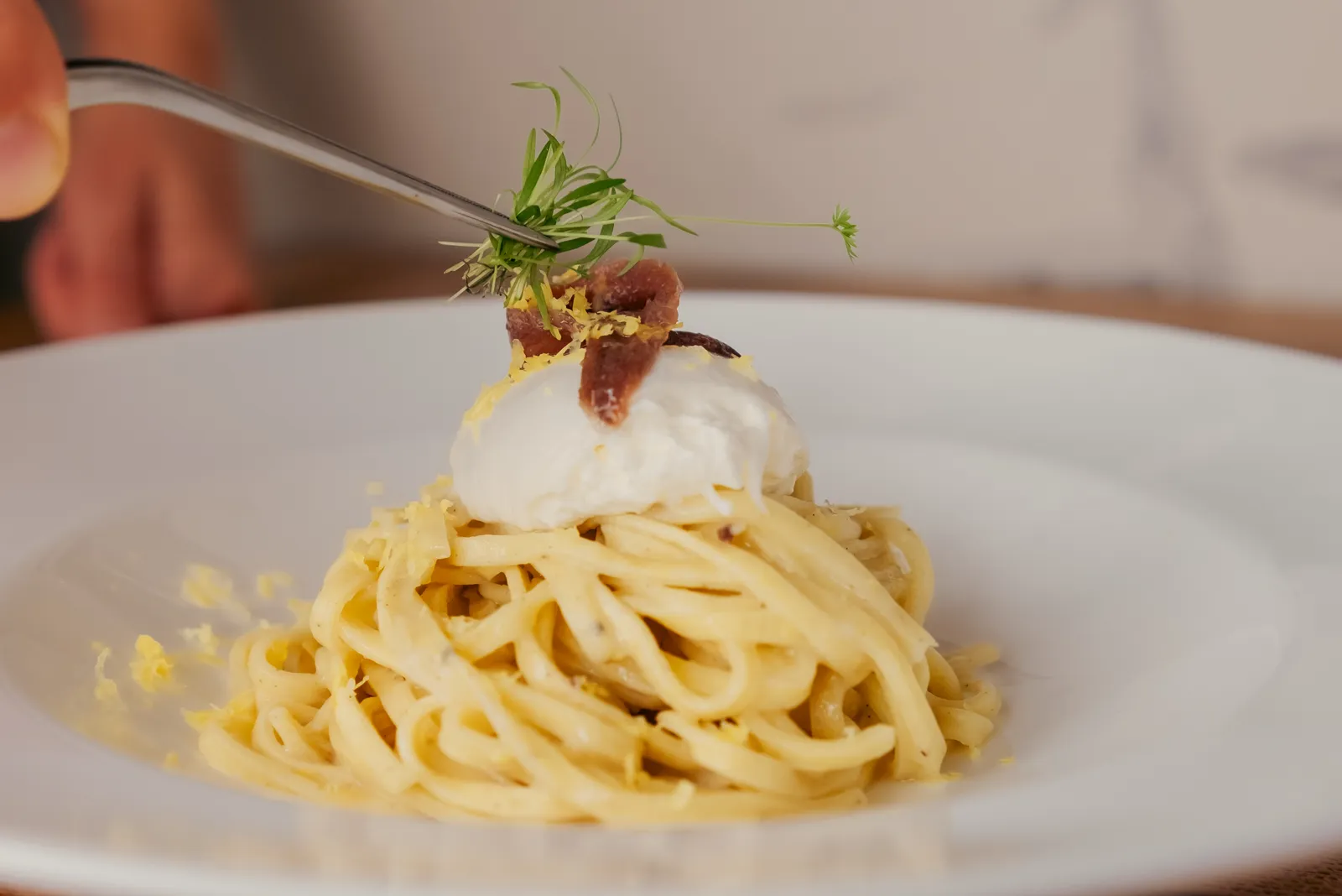 A plate of thick spaghetti being finished with herbs
